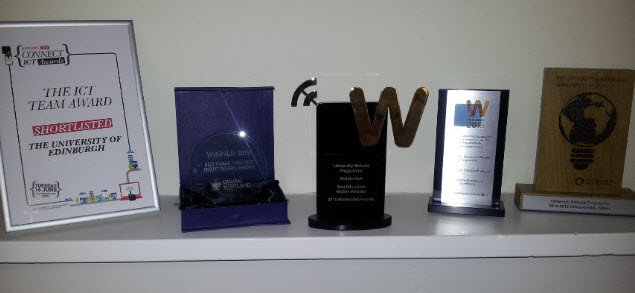 Five award trophies and certificates on a shelf in our offices