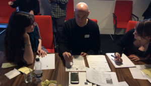 Person interacts with paper interface while two others watch and make notes
