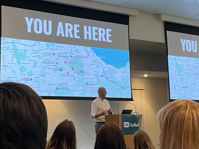 Ben presenting in front of a slide showing a map and the words you are here in capital letters