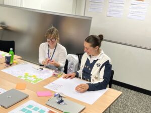 Two students smiling as they work on their sketches in the workshop.