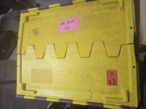 the top of a large packing crate, the top is yellow and the sides purple. red and pink stickers with WAC written on them are stuck to it