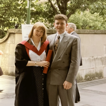 An image of a new graduate and her partner standing together with a graduation scroll