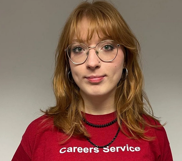 Headshot of a woman with red hair wearing glasses and a red t-shirt that reads Careers Service