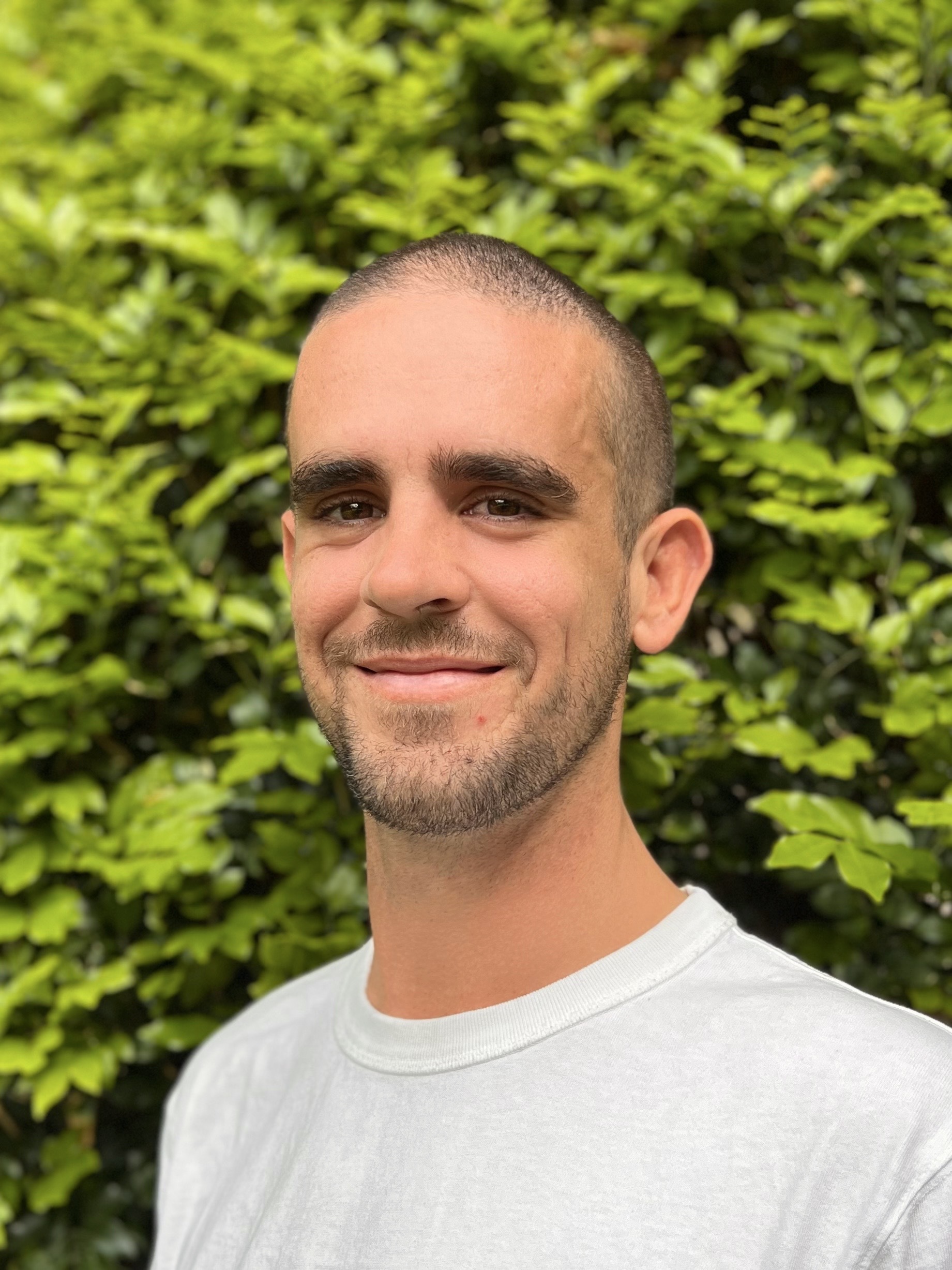 Headshot of man infront of a green bush