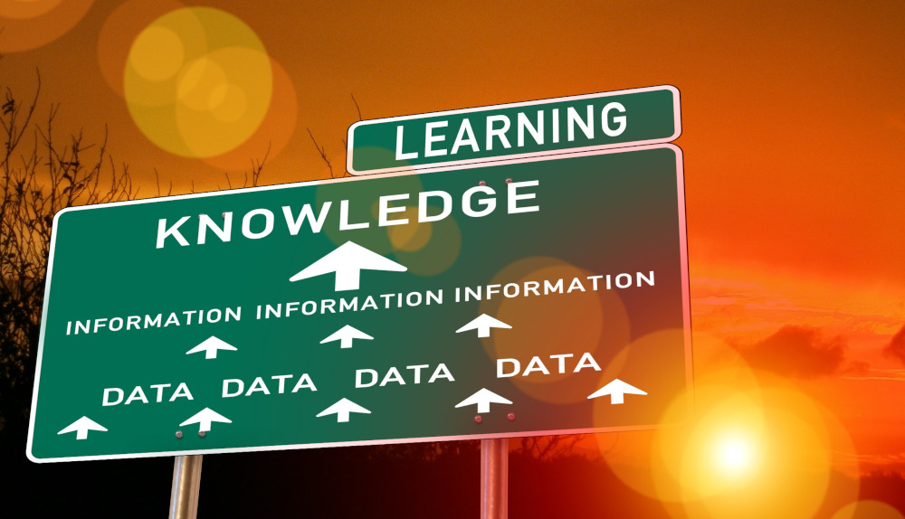 Image of a road sign with 'data' and arrow to word 'information' then arrow to word 'knowledge', and then the word 'learning' - with sunset behind.