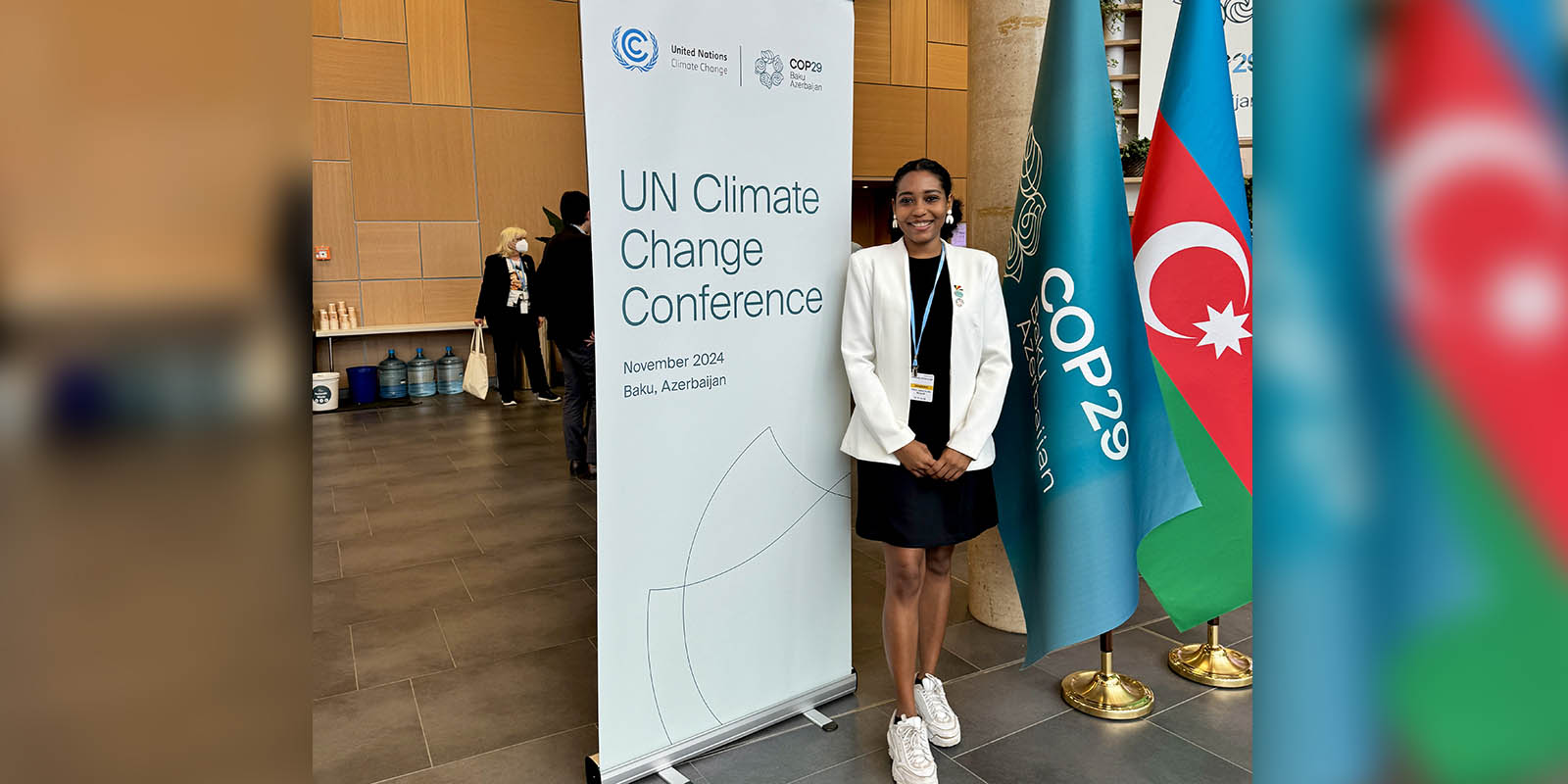 Axelle standing inside a large open space next to a pop up roller banner and two flags.