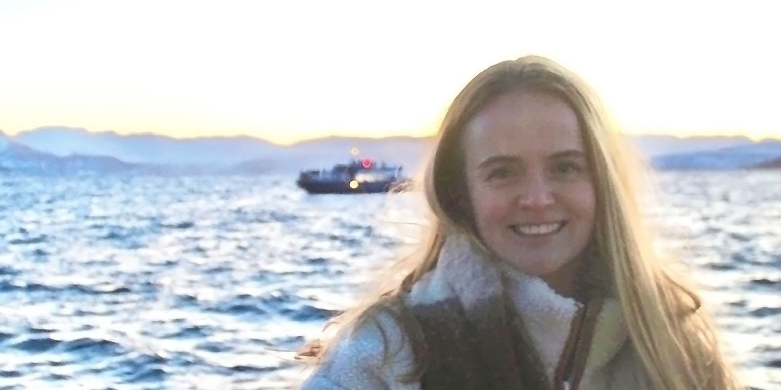 Allie stood in front of the sea with a boat in the distance.