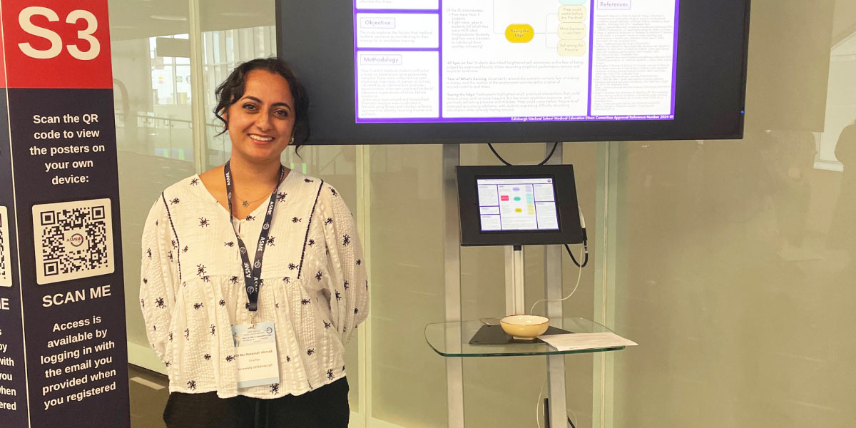 Muz wearing a lanyard and standing in front of a screen display showing academic materials.