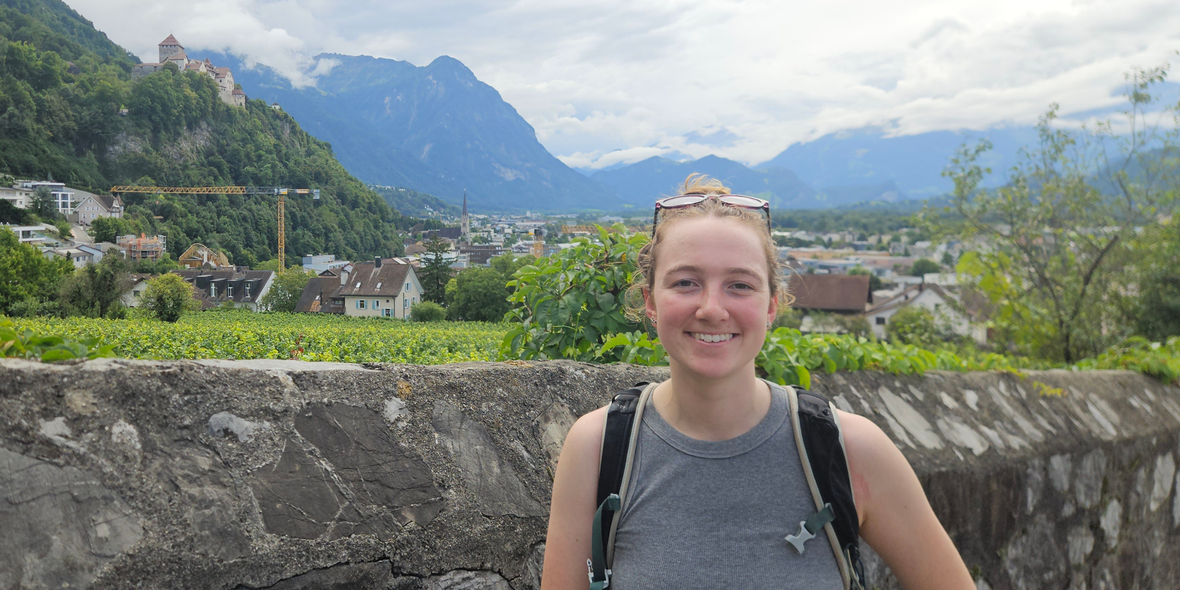 A person smiling for a photograph with mountains and greenery in the background.